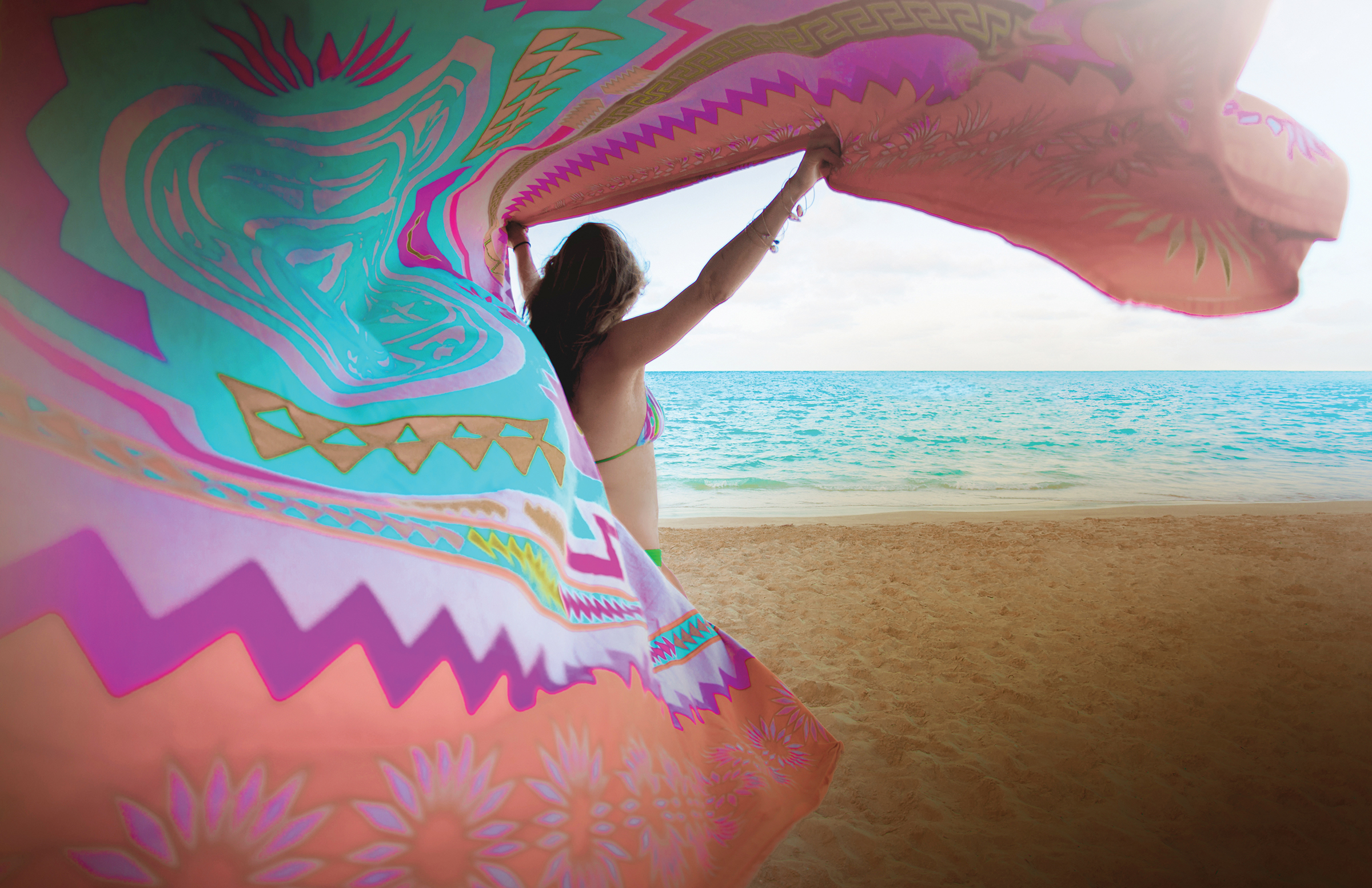 A woman on a beach waving a colorful sarong