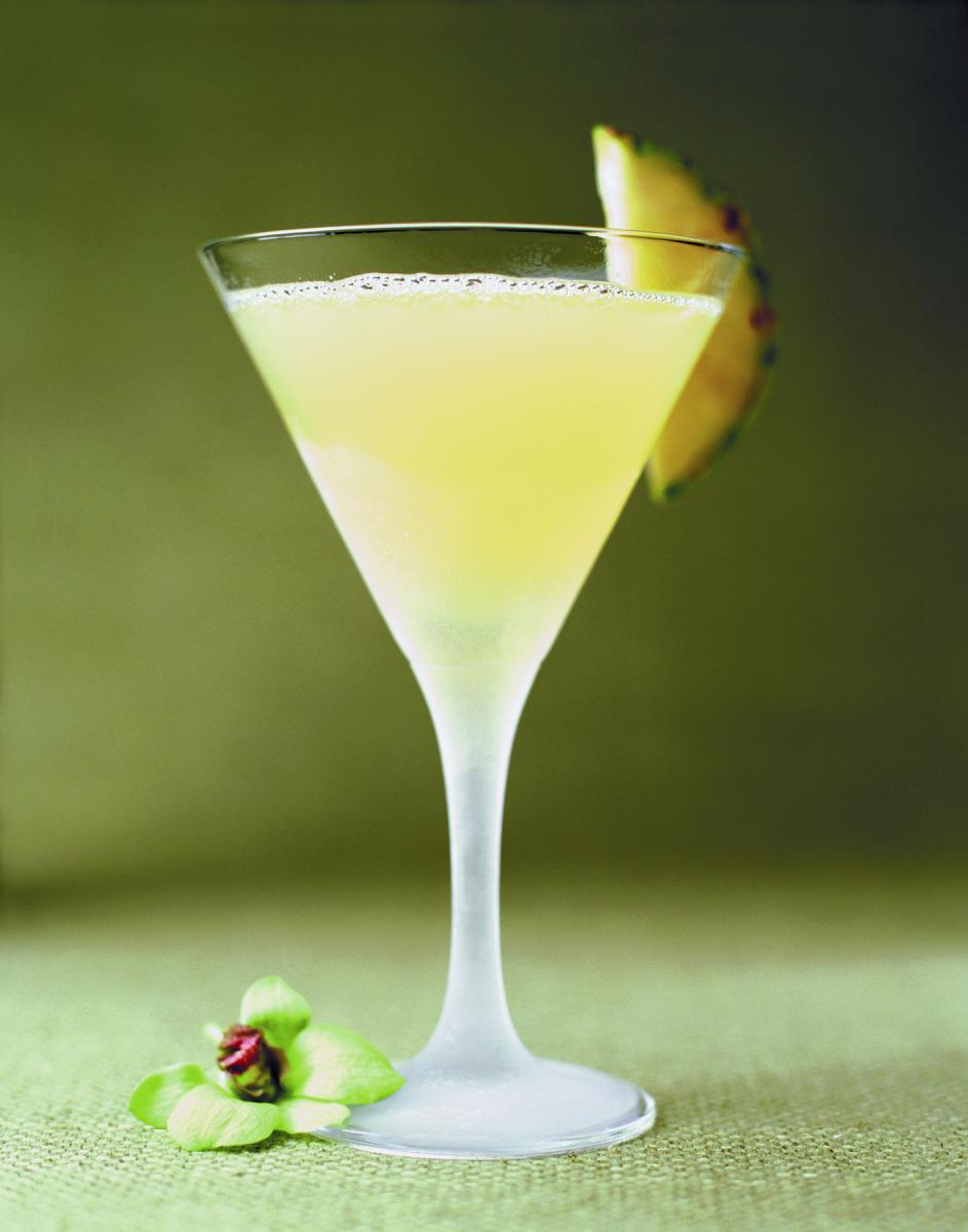 A yellow cocktail in a martini glass garnished with pineapple