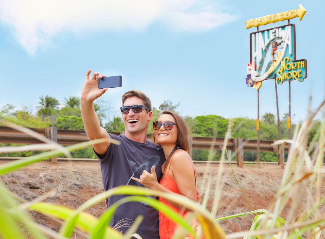 A couple taking a selfie in front of the Haleiwa sign in Oahu