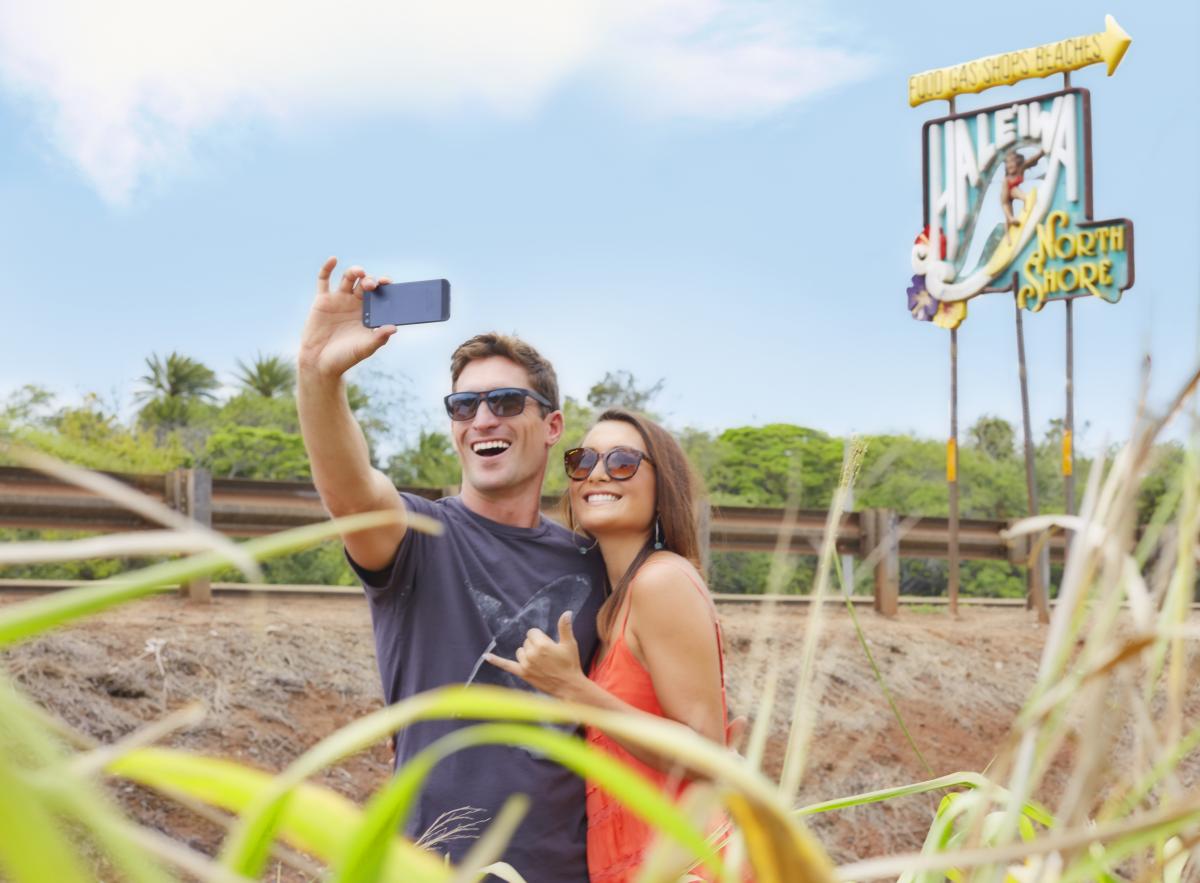 A couple taking a selfie in front of the Haleiwa Town sign in Oahu