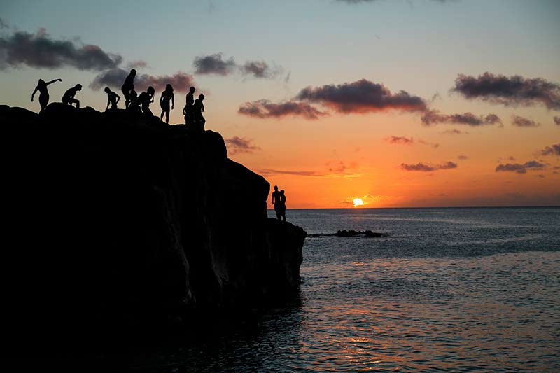 Silhouettes of people standing on a large rock watching the sunset
