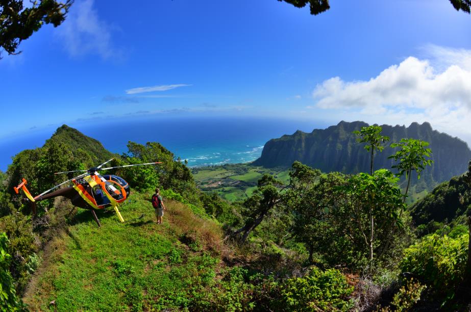 A man standing near a helicopter overlooking Kualoa Ranch, Oahu