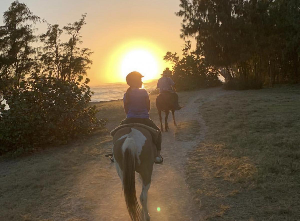 A couple riding horses into the sunset
