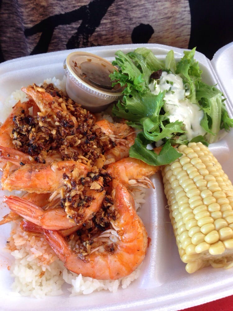 A take-out container with rice, seafood, corn, and salad