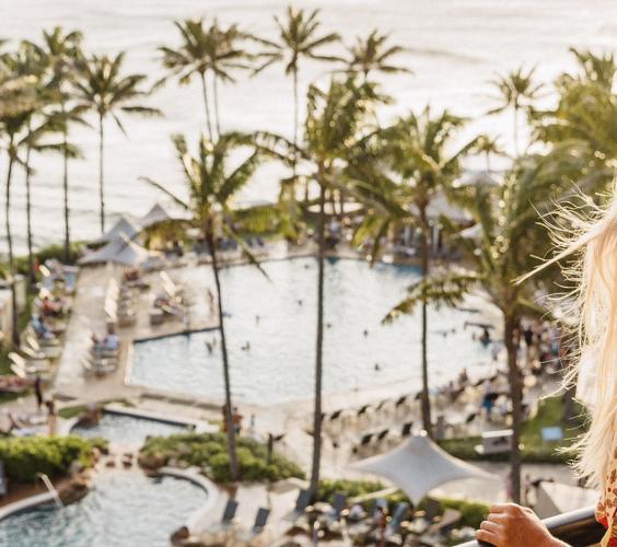 A woman stands on her balcony looking out at the ocean from her view at the resort.