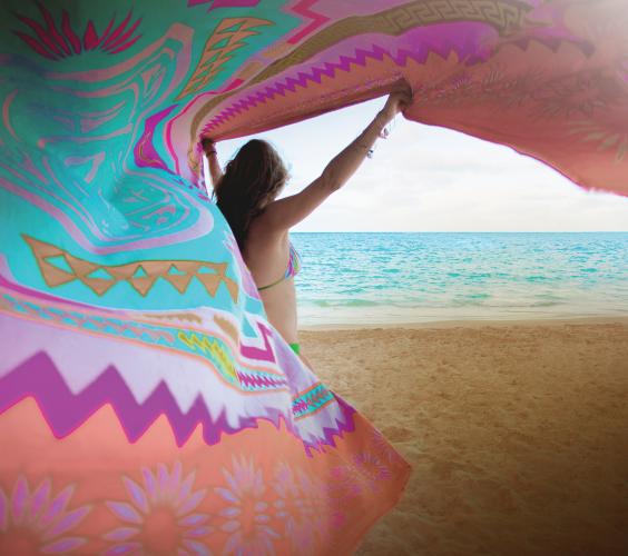 A woman on a beach waving a colorful sarong