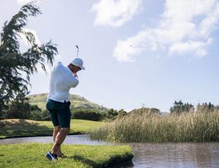 Man mid golf swing on lush green course