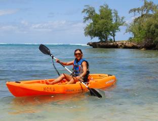 A woman in an orange kayak paddling just off shore.