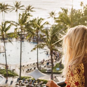 A woman stands on her balcony looking out at the ocean from her view at the resort.